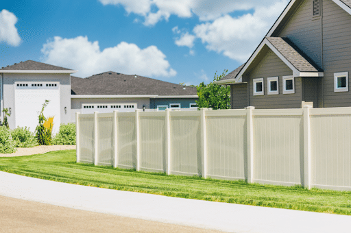 A white fence stands in front of a charming house, creating a picturesque scene. Constructed by Butte Fence.
